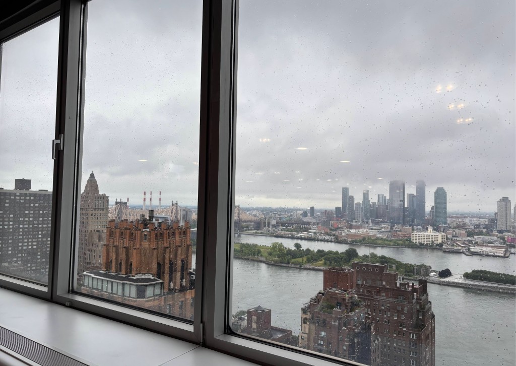 Rain-streaked windows at the German house frame a view of the East River, Roosevelt Island, and the New York City skyline on an overcast morning during UN Open Source Week.